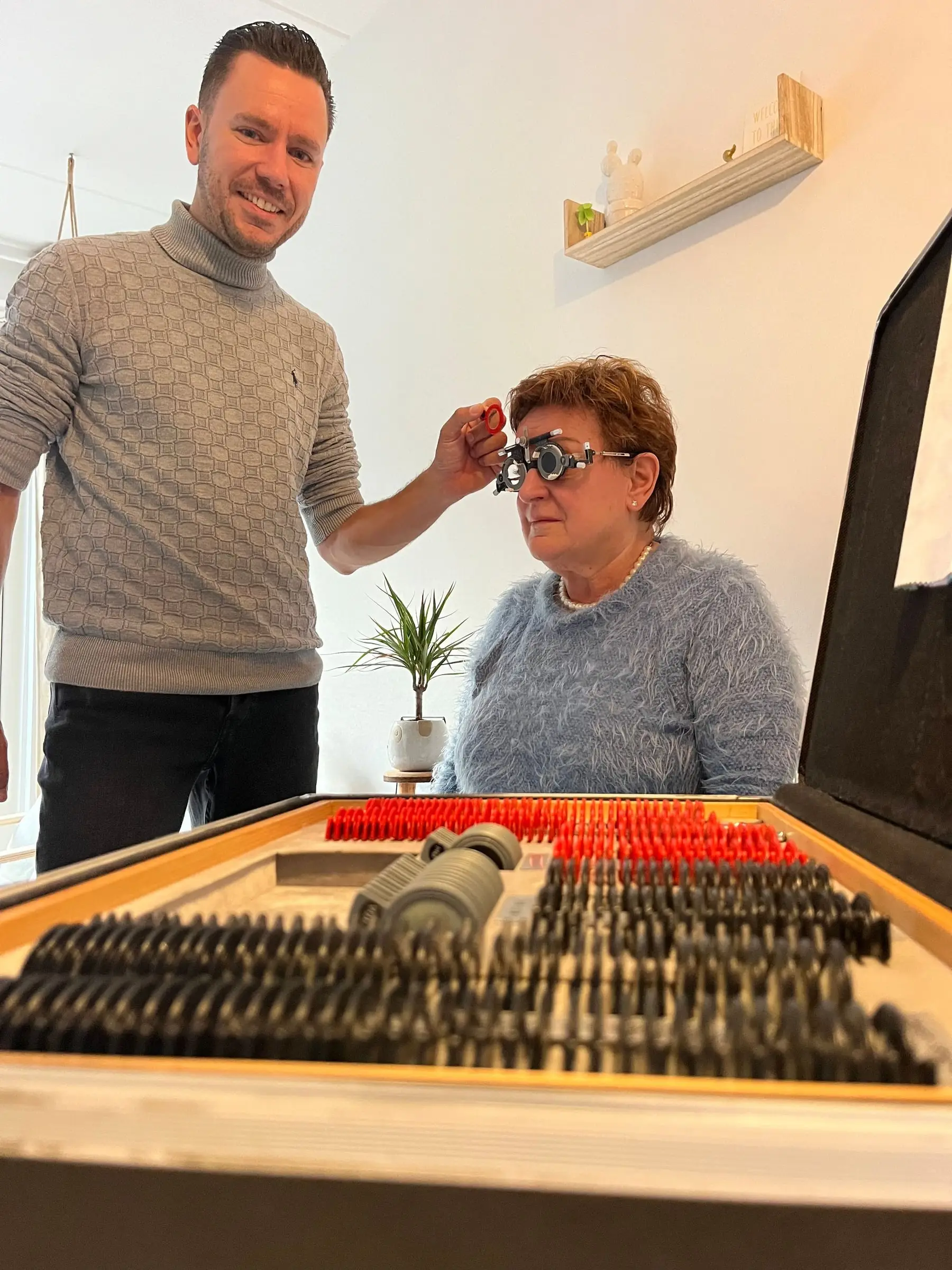 Paul meet met een pasbril bij een klant aan tafel, met de kist pasglazen ervoor